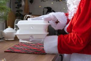 la livraison de nourriture dans des conteneurs de service à domicile entre les mains du père noël le met sur la table de la cuisine et l'emporte. commande chaude prête à l'emploi, restauration de vacances de noël et du nouvel an. photo