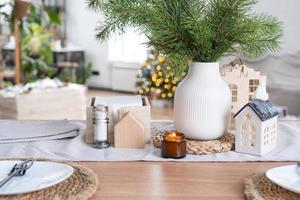 décor de noël festif dans une cuisine blanche, petit-déjeuner festif, intérieur scandi blanc. la figure d'une maison confortable sur la table dressée. nouvel an, humeur, maison confortable. copie espace photo