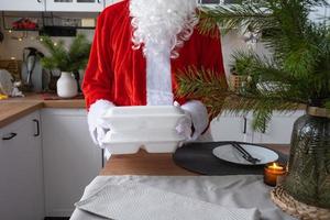 la livraison de nourriture dans des conteneurs de service à domicile entre les mains du père noël le met sur la table de la cuisine et l'emporte. commande chaude prête à l'emploi, restauration de vacances de noël et du nouvel an. photo