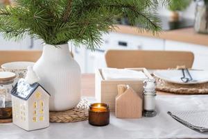 décor de noël festif dans une cuisine blanche, petit-déjeuner festif, intérieur scandi blanc. la figure d'une maison confortable sur la table dressée. nouvel an, humeur, maison confortable. copie espace photo