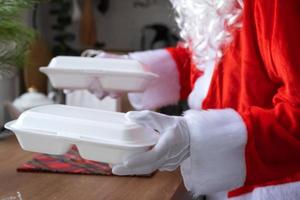 la livraison de nourriture dans des conteneurs de service à domicile entre les mains du père noël le met sur la table de la cuisine et l'emporte. commande chaude prête à l'emploi, restauration de vacances de noël et du nouvel an. photo