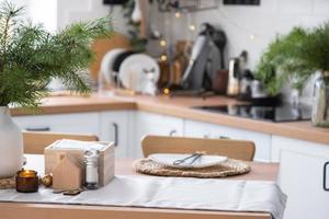 décor de noël festif dans une cuisine blanche, petit-déjeuner festif, intérieur scandi blanc. la figure d'une maison confortable sur la table dressée. nouvel an, humeur, maison confortable. copie espace photo