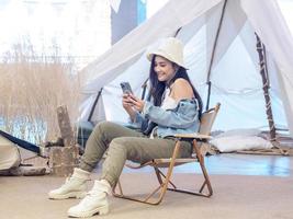 portrait belle jeune fille femme asiatique joli sourire une personne seule assise sur une chaise camping avec une tablette connectée à internet pour travailler. voyage voyage devant la tente liberté se détendre heureux profiter photo