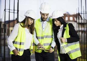 des spécialistes inspectent un chantier de construction de bâtiments commerciaux et industriels. projet immobilier avec ingénieur civil, investisseur utilise un ordinateur portable. dans la grue de fond, cadres de coffrage en béton de gratte-ciel photo