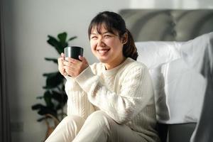 jeune femme buvant du café dans la chambre, tenant une tasse de café à deux mains photo