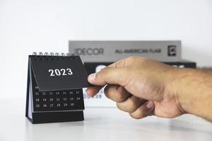 main tenant le calendrier d'affaires 2023 sur la table de bureau le jour du nouvel an. établir un plan de travail pour le début de l'année. concept sur la célébration, les affaires, noël, nouvel an. photo