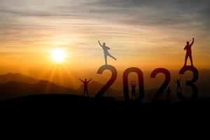 l'homme lève deux mains succès concept de bonne année 2023, silhouette d'homme sautant par-dessus la falaise de barrière et succès avec fond de coucher de soleil. bonne année 2023 à utiliser pour la bannière web et la publicité. photo