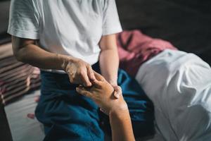 massage et spa traitement relaxant du syndrome de bureau style de massage thaï traditionnel. asain masseuse féminine senior faisant un massage traiter la main, les maux de dos, les douleurs au bras, le pied et le stress pour la vieille femme fatiguée. photo