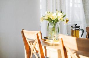 beau bouquet de tulipes jaunes dans un vase sur la table du dîner dans l'intérieur lumineux de la cuisine blanche à la maison photo