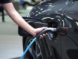 Tenir la main du véhicule de charge électrique pour recharger la batterie de la voiture de couleur noire pour l'énergie propre de l'avenir concept photo