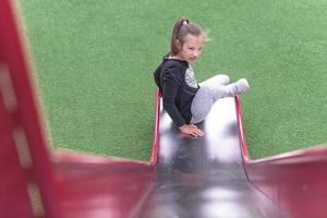 cri du chat, une fille autiste glisse dans une aire de jeux pour enfants située dans un parc public. photo