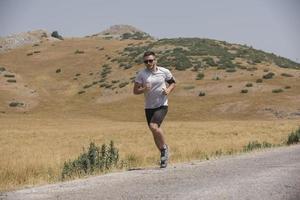 coureur de jeune homme courant sur une route de montagne. séance d'entraînement de jogger dans une chaussure de fitness. mode de vie sain et concept sportif. flou de mouvement et mise au point sélective. photo