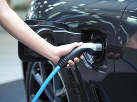 Tenir la main du véhicule de charge électrique pour recharger la batterie de la voiture de couleur noire pour l'énergie propre de l'avenir concept photo