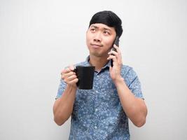 homme asiatique tenant une tasse de café et parlant avec un geste de téléphone portable heureux photo