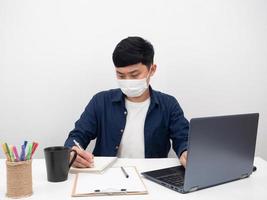 homme portant un masque de protection écrivant sur un ordinateur portable et utilisant un ordinateur portable sur le lieu de travail de bureau photo
