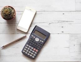 Smartphone écran blanc avec cactus et argent stylo et calculatrice sur table en bois blanc vue de dessus copie espace soleil ombre concept d'entreprise photo