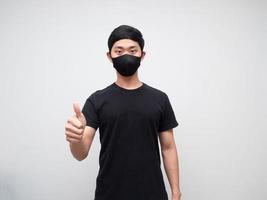 homme asiatique portant un masque de protection montrer le pouce vers le haut en regardant la caméra sur fond blanc photo