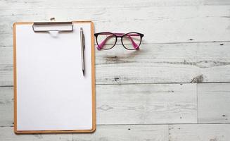 Stylo argenté sur feuille de document presse-papiers en bois avec des lunettes sur une table en bois blanc vue de dessus l'ombre de la nature de l'espace photo