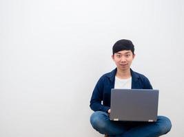 Asian man happy face using laptop assis sur la chaise sur fond de mur blanc photo