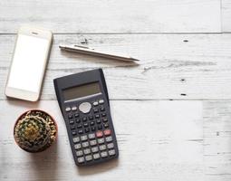 Smartphone écran blanc avec cactus et argent stylo et calculatrice sur table en bois blanc vue de dessus copie espace soleil ombre concept d'entreprise photo