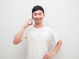 Homme asiatique beau téléphone portable parlant avec un sourire heureux sur fond de mur blanc photo