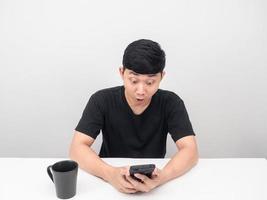 homme assis à table avec une tasse de café tenant un téléphone portable émotion excitée photo