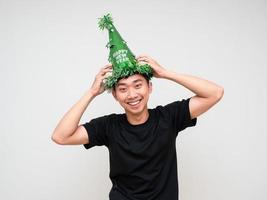 jeune homme chemise noire toucher chapeau vert sur la tête sourire heureux regarder la caméra sur fond blanc célébration bonne année concept photo