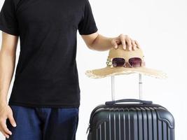 L'homme chemise noire se tient debout avec des lunettes de soleil chapeau suspendu au-dessus des bagages sur blanc isolé,voyage vacances concept photo