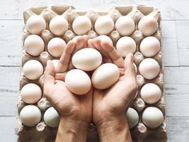 trois oeufs de canard à la main sur des oeufs de canard de groupe dans une boîte en carton avec la lumière et l'ombre de la nature sur fond de bois blanc vue de dessus photo