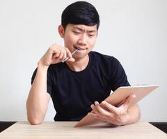 jeune homme avec stylo pense et visage sérieux avec le livre sur le bureau regarde la caméra sur blanc isolé, concept de livre d'étude photo