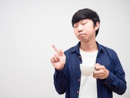 homme endormi tenant une tasse de café fermer les yeux et pointer du doigt l'espace de copie fond blanc photo