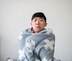 jeune homme se sentir malade triste au visage couvrir son corps par une couverture sur fond blanc isolé, concept d'homme malade photo
