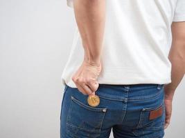 gros plan sur le dos de l'homme ramasser du bitcoin doré dans la poche de jean du pantalon photo