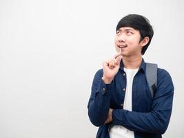 homme asiatique avec sac à dos stylo morsure visage sérieux pensant quelque chose regarder l'espace fond blanc photo