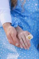 concept de rendez-vous romantique. mains de jeune homme et femme se tenant. fille avec bague dorée au doigt en robe bleue avec fleur de camomille à la main photo