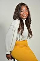 portrait d'une belle femme afro-américaine positive en jupe jaune et chemise blanche debout et posant en studio photo
