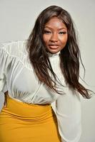 portrait d'une belle femme afro-américaine positive en jupe jaune et chemise blanche debout et posant en studio photo