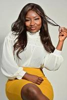 portrait d'une belle femme afro-américaine positive en jupe jaune et chemise blanche debout et posant en studio photo