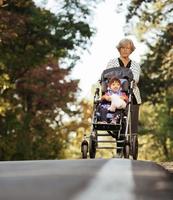 heureuse dame âgée poussant le fauteuil roulant et les enfants. grand-mère et enfants profitant d'une promenade dans le parc. enfant à charge d'un grand-parent handicapé. visite de la famille. générations amour et relation photo