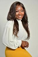 portrait d'une belle femme afro-américaine positive en jupe jaune et chemise blanche debout et posant en studio photo