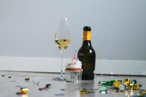 bouteille et verre de champagne et cupcake avec bougie sur le sol avec des confettis après la fête d'anniversaire à la maison photo