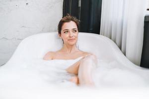 jeune femme heureuse prenant un bain avec de la mousse à la maison, faites-vous plaisir photo