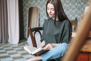 jeune femme souriante adolescente étudiante aux cheveux longs noirs dans un livre de lecture décontracté à la maison photo