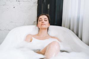 jeune femme heureuse prenant un bain avec de la mousse à la maison, faites-vous plaisir photo