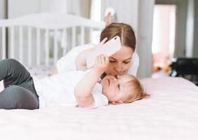 jeune mère embrassant une jolie petite fille avec un téléphone portable sur le lit à la maison photo