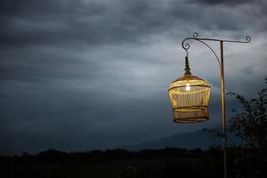 cage à oiseaux blanche comme lampe contre le ciel sombre photo