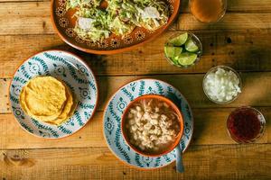 pozole servi dans un plat profond, avec tostadas, salsa et légumes sur une table en bois. cuisine mexicaine typique. photo