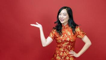 femme asiatique avec cheongsam rouge ou qipao pointant vers le présent pour les vacances de célébration du nouvel an chinois isolé sur fond rouge concept photo
