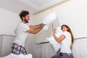 heureux jeune couple s'amuse au lit. appréciant la compagnie les uns des autres. bataille d'oreillers couple drôle se battant avec des oreillers au lit photo