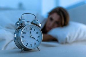 insomnie et désespérée belle femme caucasienne éveillée la nuit incapable de dormir, se sentant frustrée et inquiète en regardant l'horloge souffrant d'insomnie dans le concept de trouble du sommeil. photo